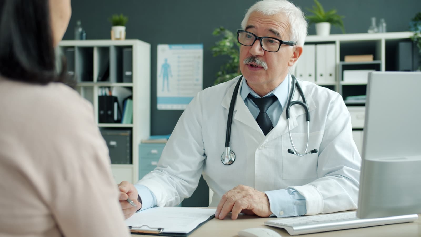 Médico conversando com a paciente no consultório, sem olhar para a tela